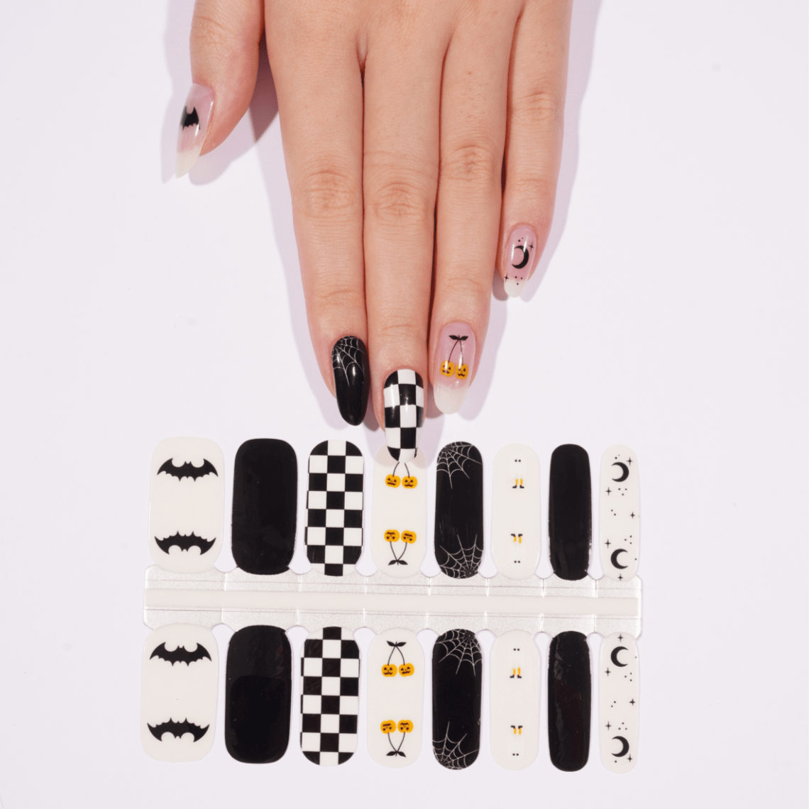 Black and white checkerboard nail wraps on hand showing Halloween bat and ghost designs