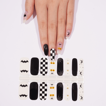 Black and white checkerboard nail wraps on hand showing Halloween bat and ghost designs