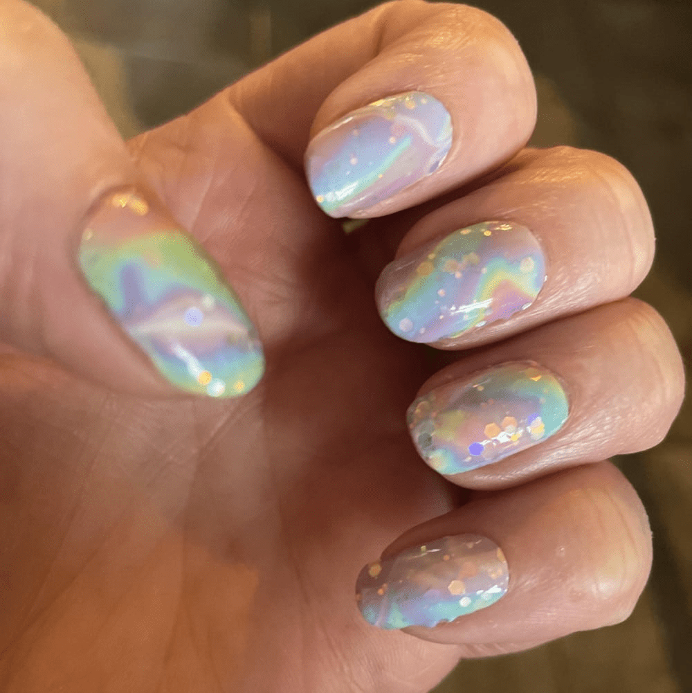 Hand wearing iridescent chrome nail wraps with aurora rainbow finish and holographic swirl design