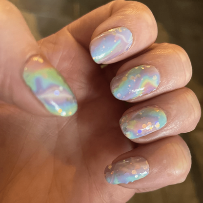 Hand wearing iridescent chrome nail wraps with aurora rainbow finish and holographic swirl design