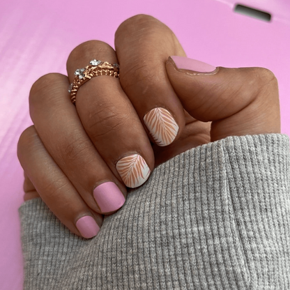 Hand wearing pink nail wraps with coral tropical fern leaf designs