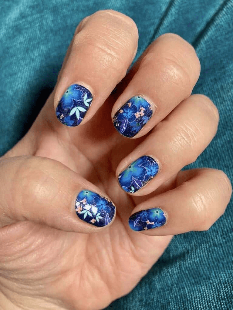 Blue floral nail wraps on hand displaying tropical garden botanical patterns