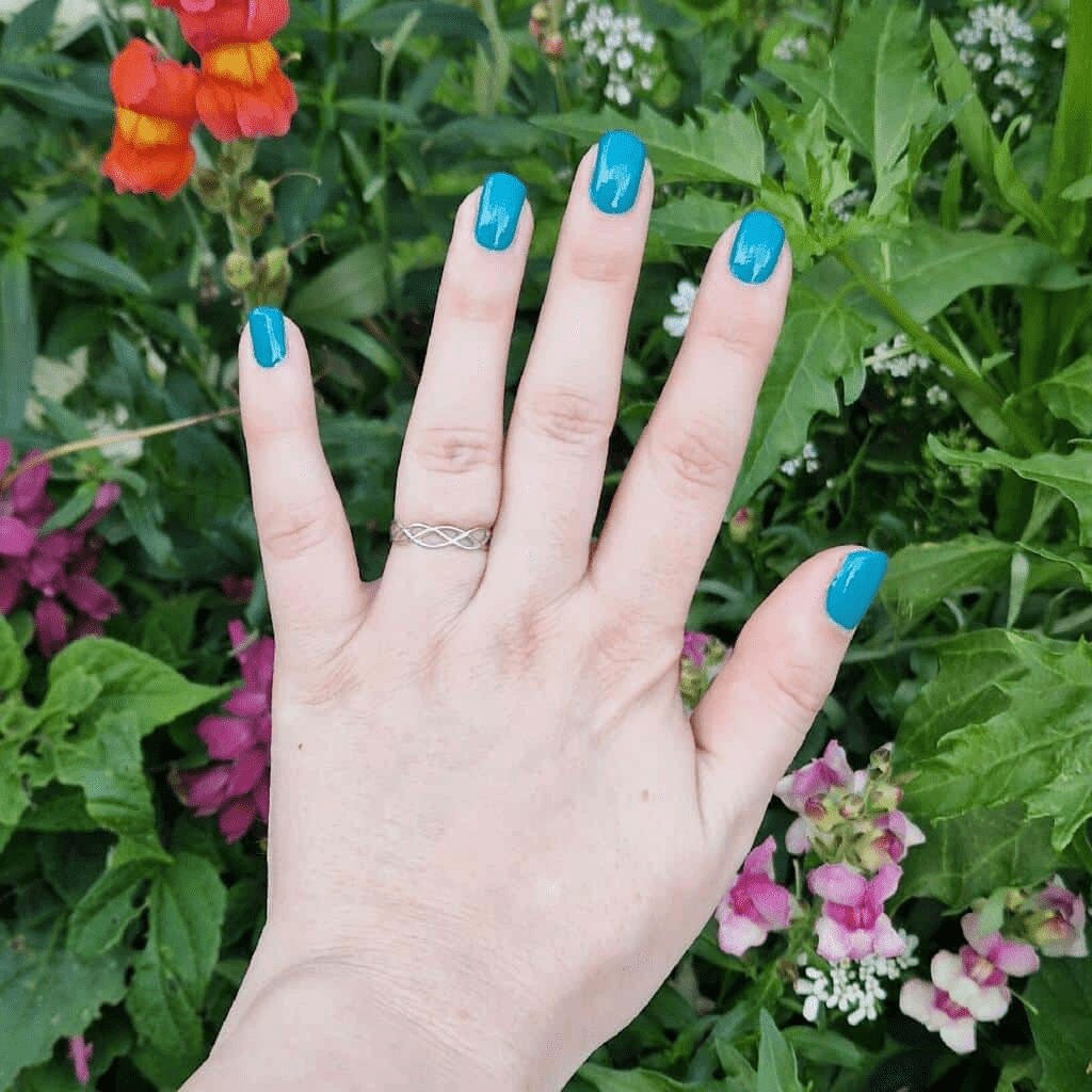 Turquoise gel nail wraps on hand against colourful garden flowers background