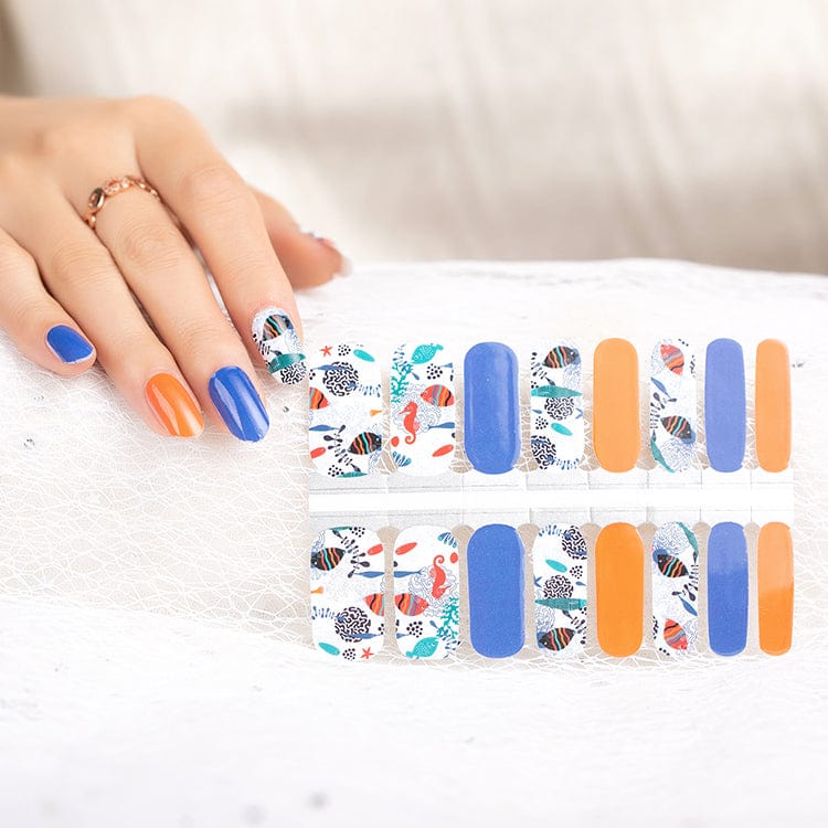 Hand applying ocean themed nail wraps with seahorse coral and blue patterns for nail art