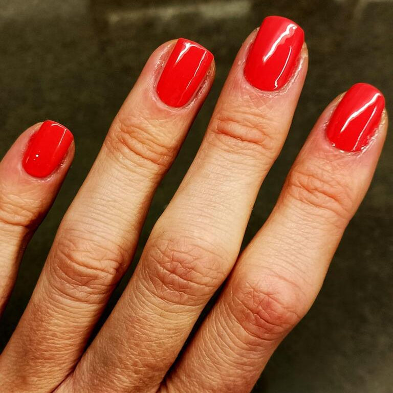 Glossy red nail wraps on hand showing classic vermillion manicure finish