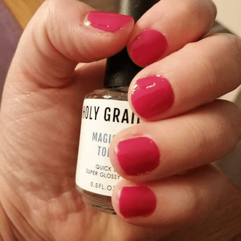 Hand holding nail care product wearing vibrant pink nail wraps manicure