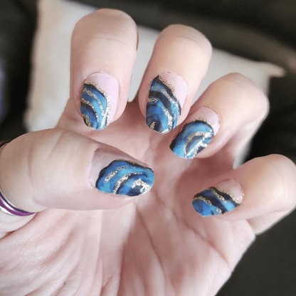 Metallic blue swirl nail art wraps on cupped hand displaying shimmery vortex pattern