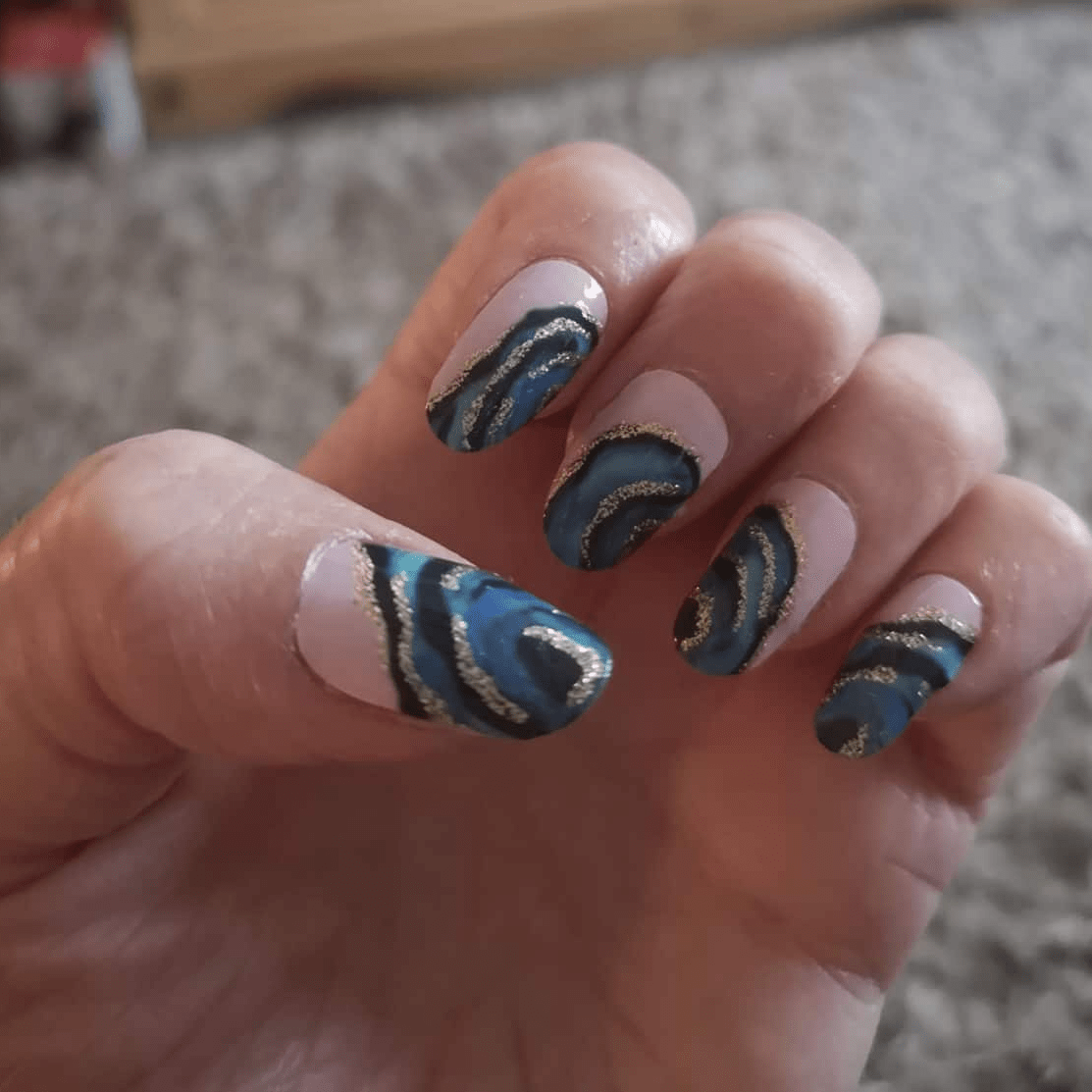 Blue gold metallic vortex nail wraps on hand showing swirling pattern design