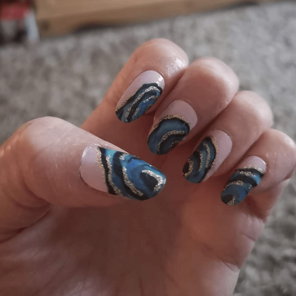 Blue gold metallic vortex nail wraps on hand showing swirling pattern design
