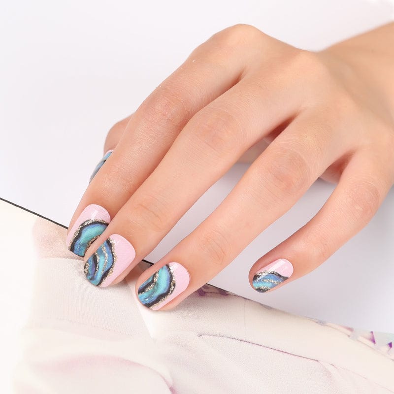 Blue and gold metallic swirl pattern nail wraps on hand showing vortex design