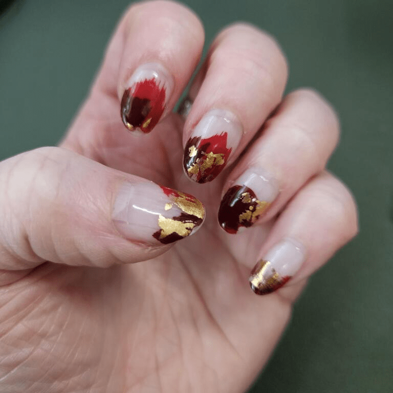 Hand displaying red gold abstract nail wraps with clear base and artistic accents