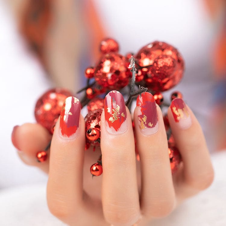 Hands with red gold nail art wraps holding festive baubles for holiday manicure