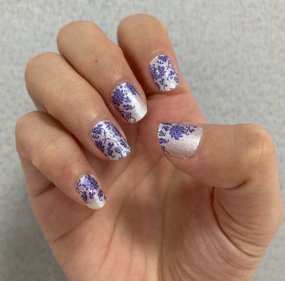 Hand displaying blue and white floral nail wraps with traditional porcelain pattern finish