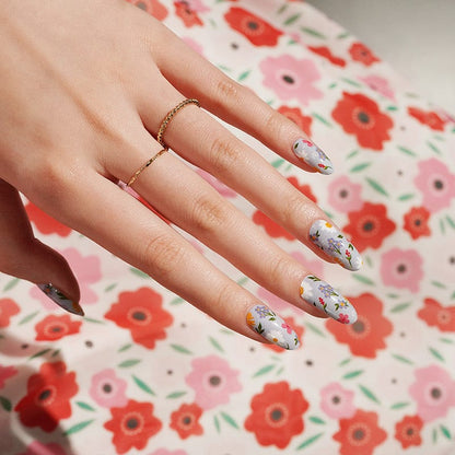 Hand wearing floral nail art wraps with botanical wildflower pattern on matching floral background