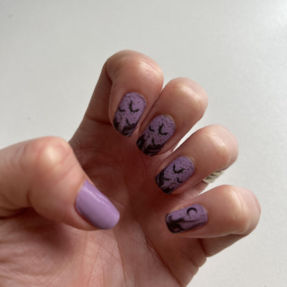 Purple ombre nail wraps with black bat silhouettes on hand showing Halloween nail art