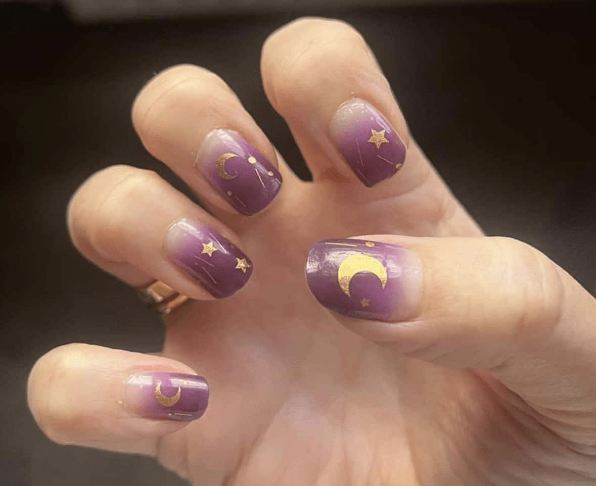 Celestial purple nail wraps with gold stars and crescent moons on hand