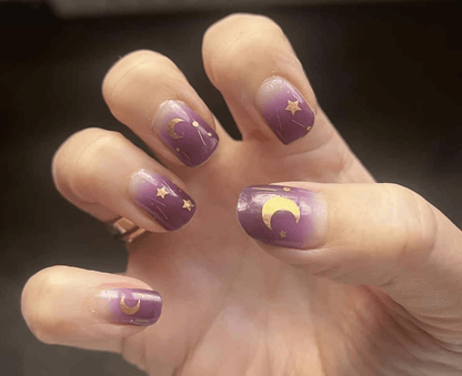 Celestial purple nail wraps with gold stars and crescent moons on hand