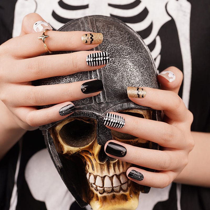 Halloween nail wraps on hands holding skull featuring black, gold, white gothic patterns and designs