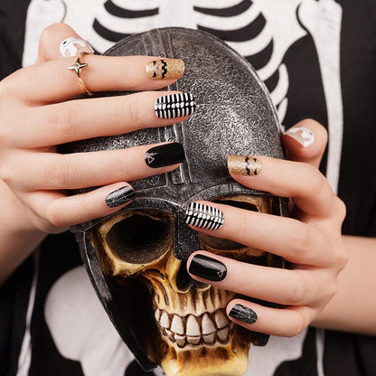 Halloween nail wraps on hands holding skull featuring black, gold, white gothic patterns and designs