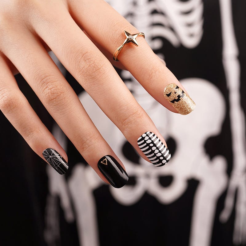 Spooky nail art wraps on hand with black, gold glitter, and Halloween pattern designs