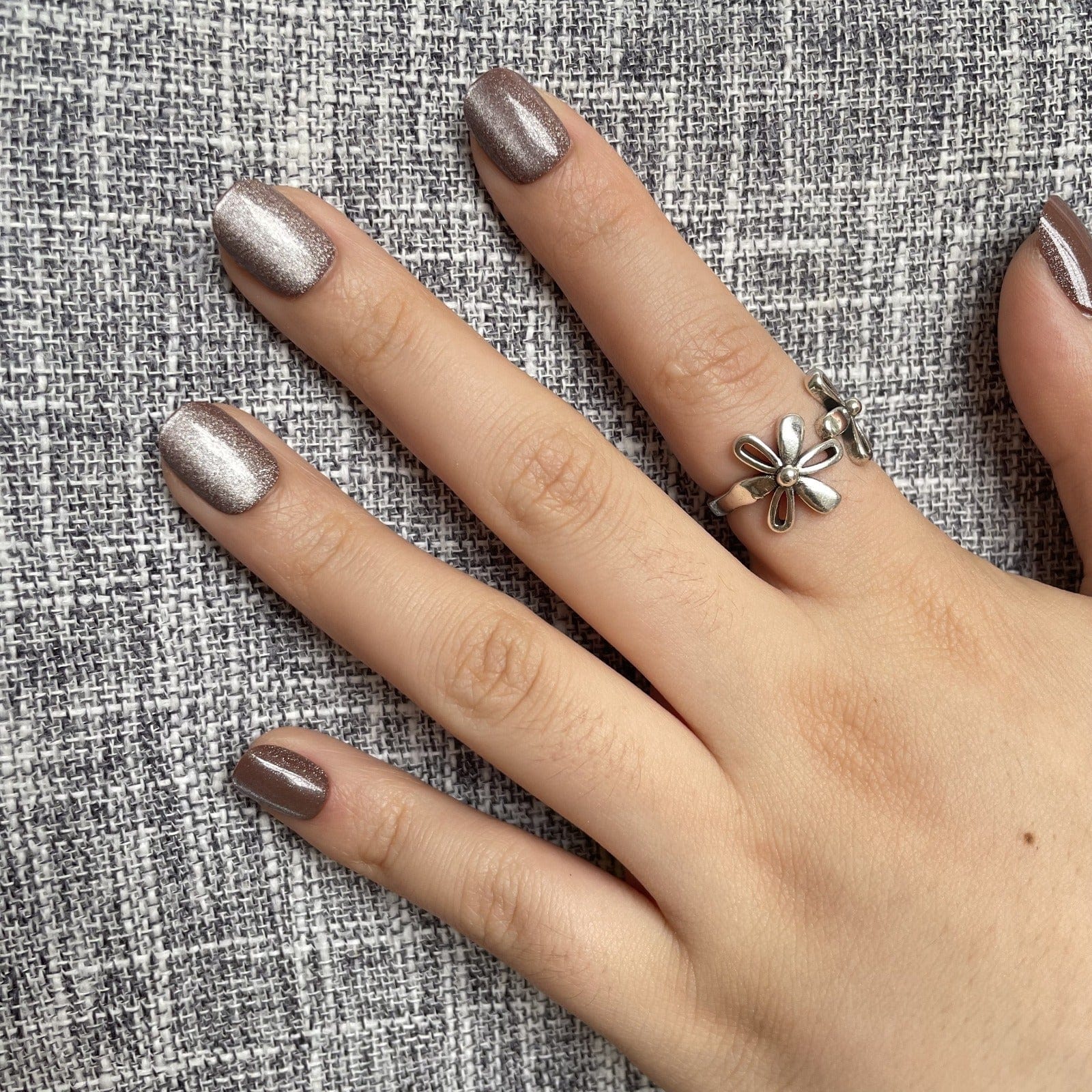 Taupe cat's eye press-on nails with shimmer finish on hand against textured grey fabric