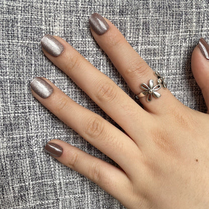 Taupe cat's eye press-on nails with shimmer finish on hand against textured grey fabric