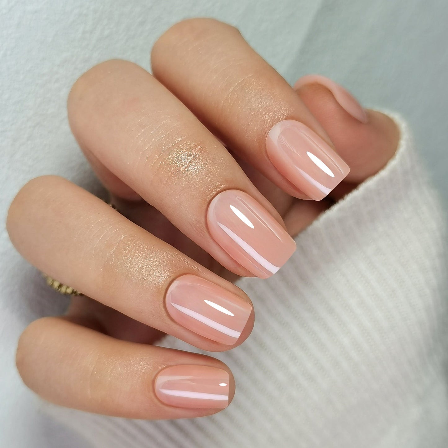 Glossy nude pink press-on nails in short square shape on hand showing glazed finish