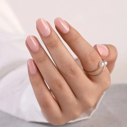 Glossy nude pink press-on nails in short oval shape on hand with ring