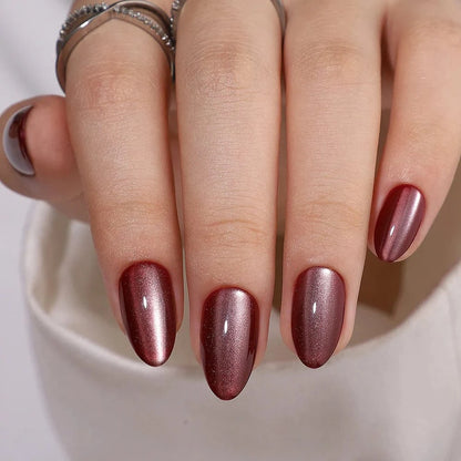 Burgundy cat's eye press-on nails in almond shape showing magnetic shimmer effect on hand