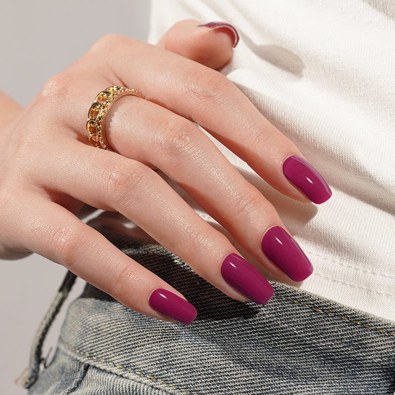Deep burgundy gel nail wraps on hand with gold chain ring showing glossy finish