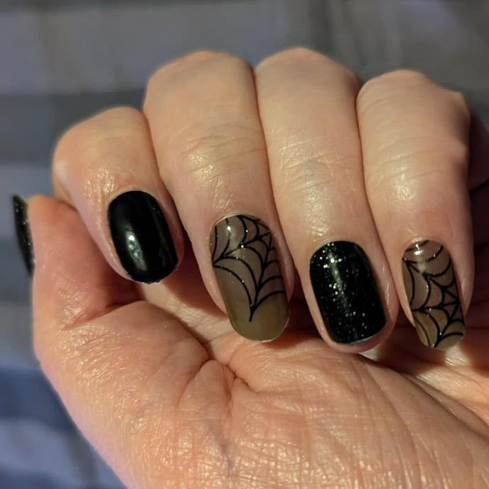 Gothic spider web gel nail wraps on hand black glitter nude manicure design