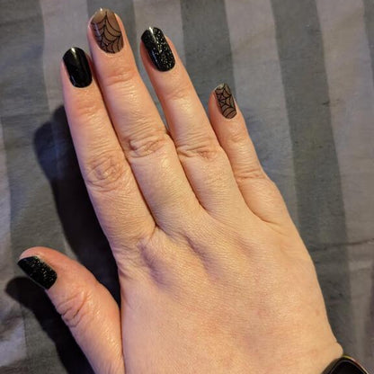 Black gel nail wraps with glitter and cobweb spider design on hand manicure