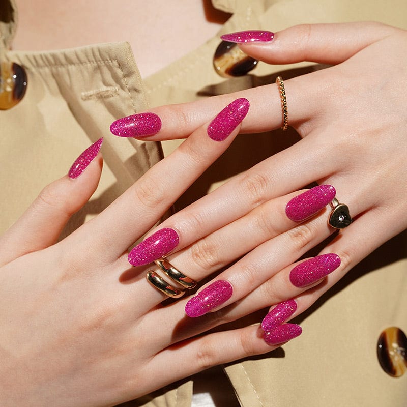 Hands showing hot pink glitter gel nail wraps with gold rings and jewellery