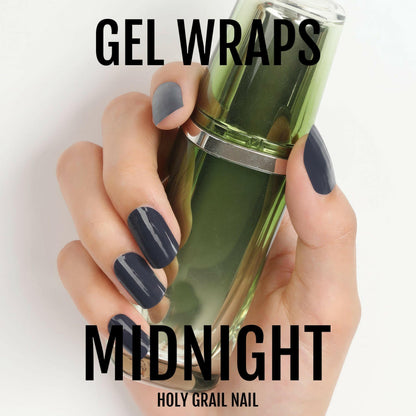 Black glossy gel nail wraps on hand holding green nail polish bottle for manicure
