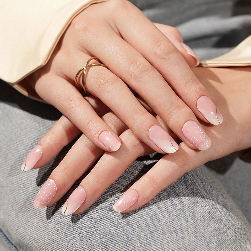 Delicate pink gel nails with glitter finish and French manicure on hands with gold rings
