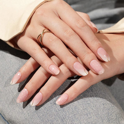Delicate pink gel nails with glitter finish and French manicure on hands with gold rings