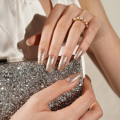 Champagne glitter gel nail wraps on hands with gold rings against sparkly textured background
