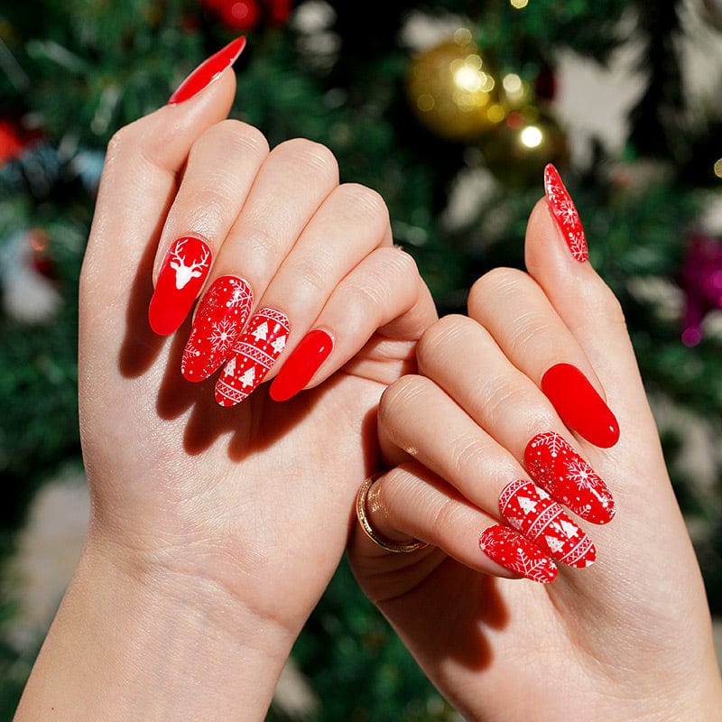 Hands showing red Christmas gel nail wraps with white reindeer and Nordic patterns