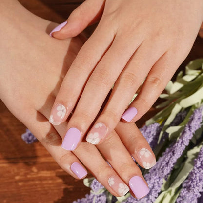 Hands wearing lilac gel nail wraps with white floral nail art for spring manicure