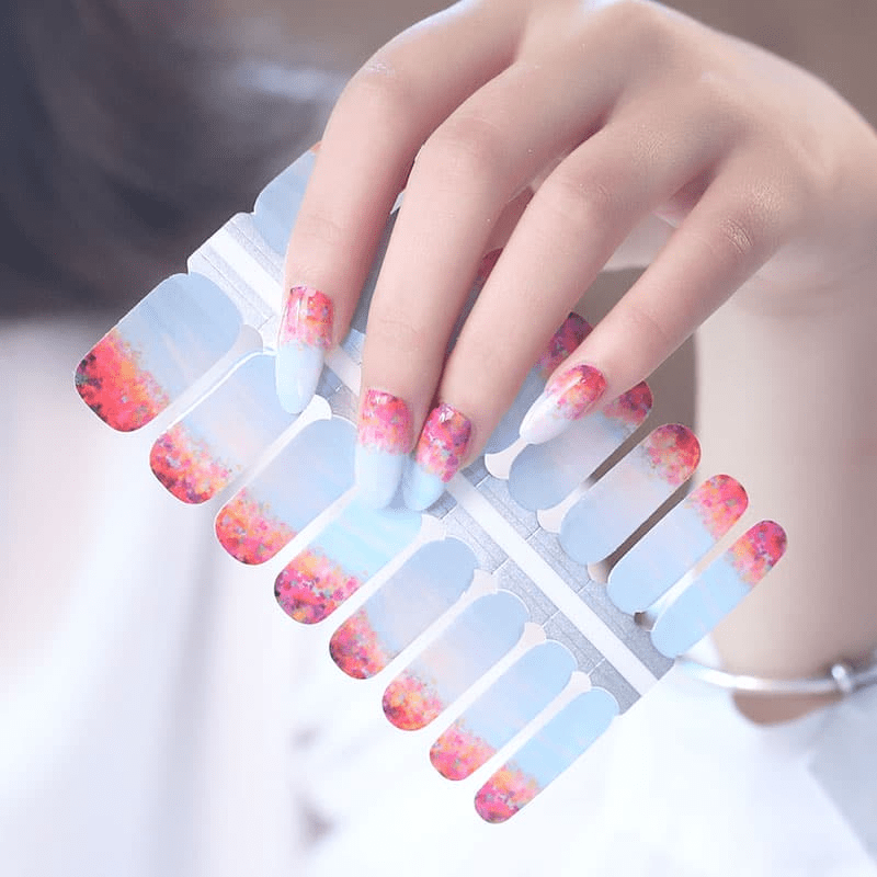 Hand holding blue and coral gradient nail wraps with watercolour pattern